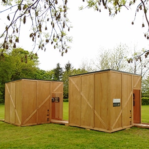Vue extérieure de 2 modules d’expo, en bois, rappelant des caisses de transport, posés dans le parc d’une abbaye