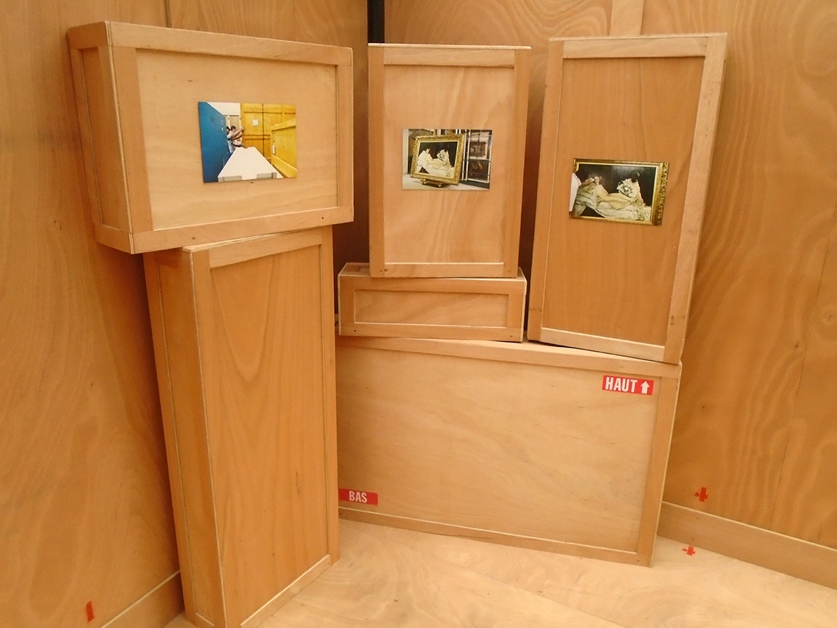 Vue intérieure d’un module d’exposition réalisé sur mesure, en bois, avec 3 œuvres de Nicolas Krief exposées sur des caisses en bois évoquant le transport d’œuvres d’art