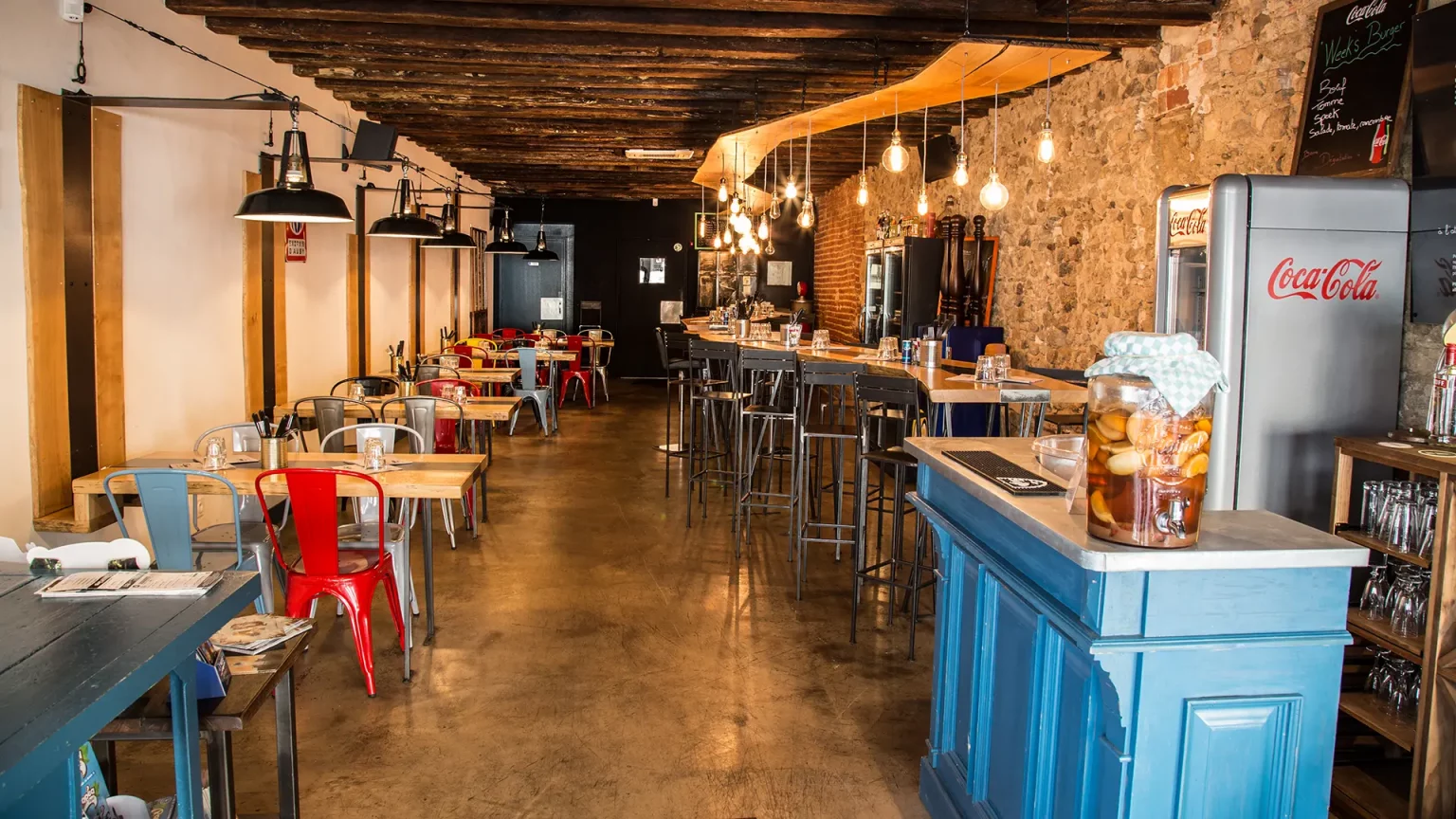 Ernestinn : salle en longueur, comptoir bleu, murs de pierre et ampoules suspendues